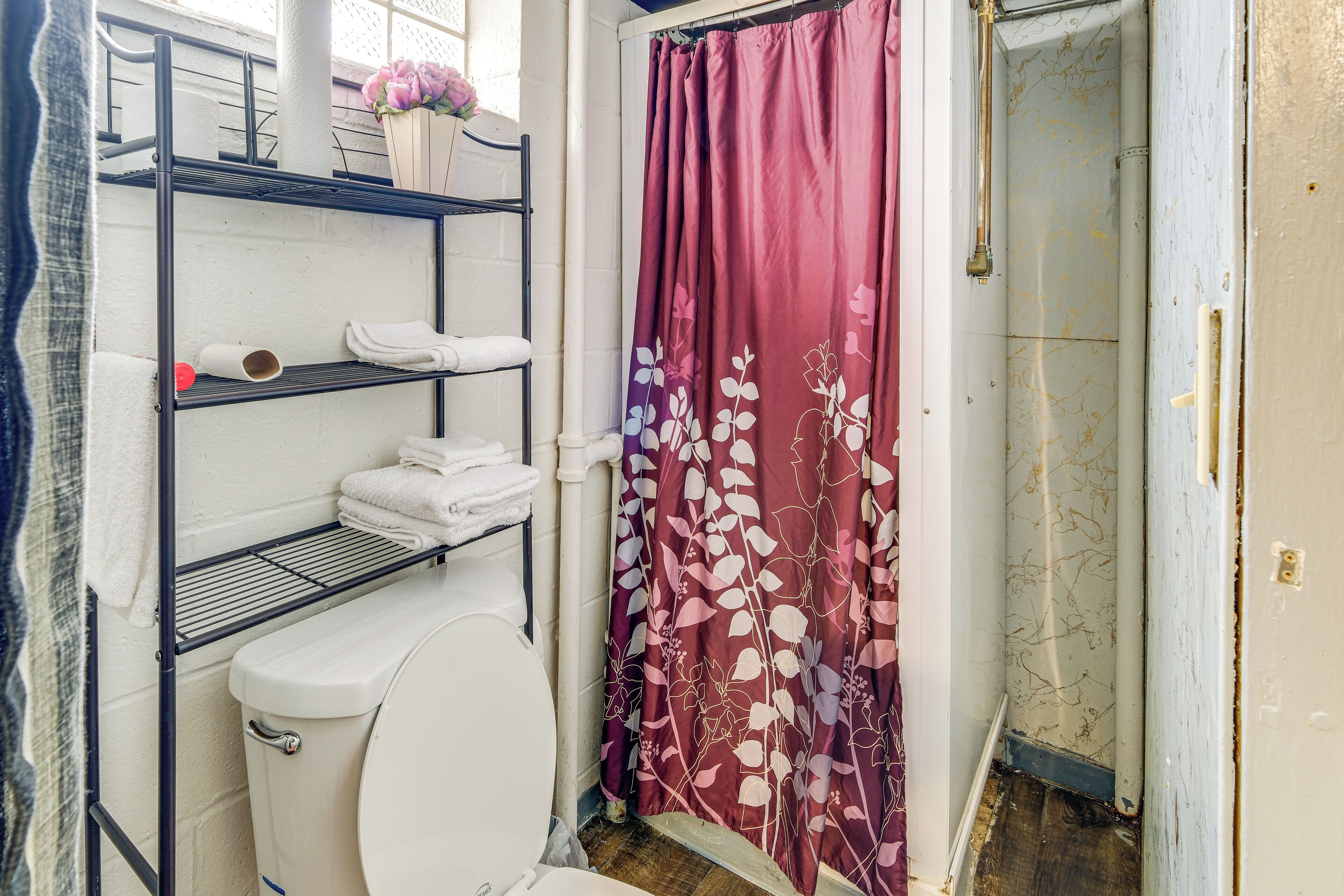 Une salle de bain avec des toilettes blanches, une étagère avec des serviettes et un rideau de douche à motifs floraux.