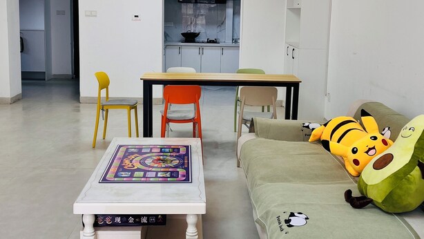 Uma sala de estar moderna com um sofá, uma mesa com jogo de tabuleiro e uma cozinha ao fundo.