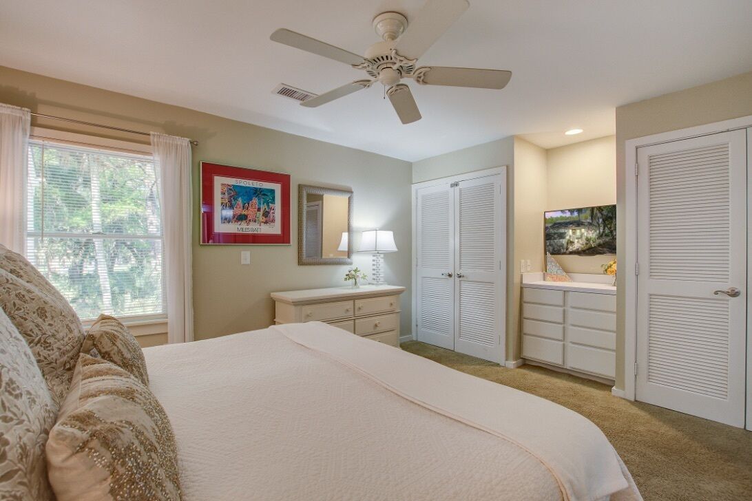 A bedroom with a bed, a ceiling fan, a dresser, a vanity, and a closet.