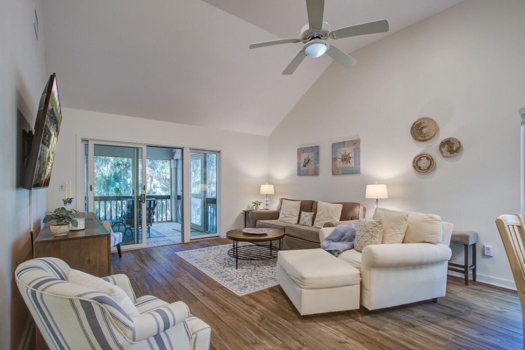 A spacious living room with a ceiling fan, a sofa set, a coffee table, and a dining area with a table and chairs.