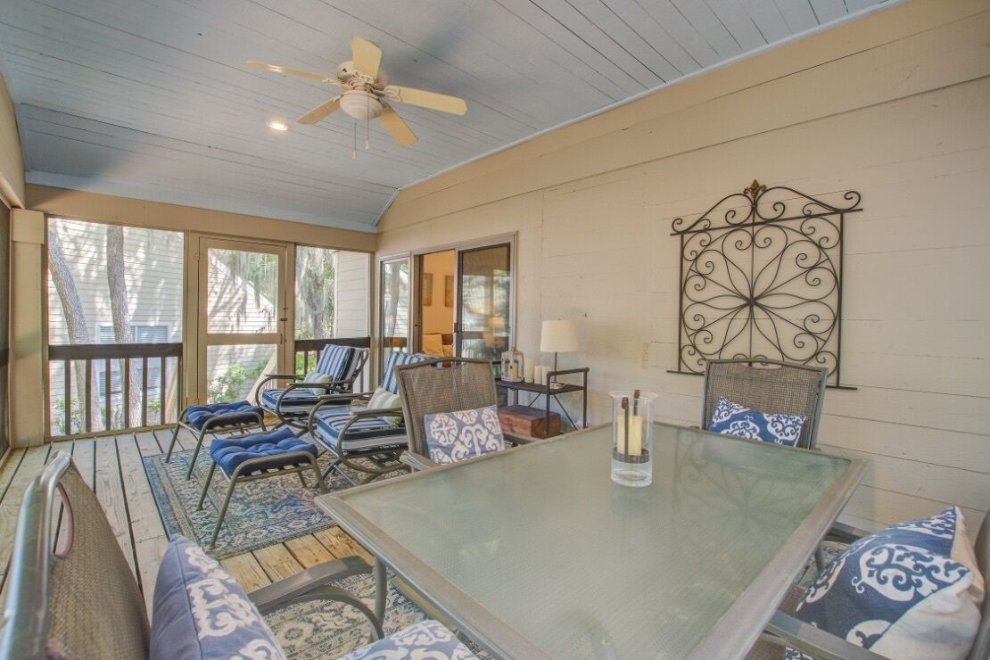A covered patio with a glass table, chairs, and a ceiling fan.