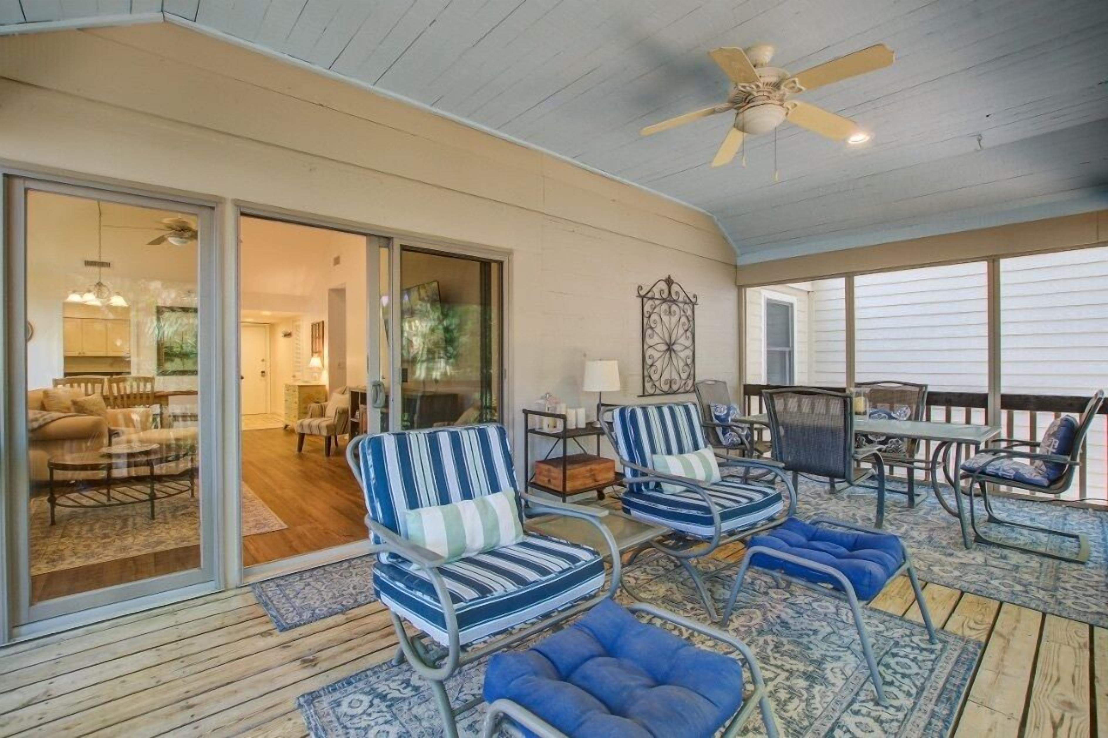 A covered outdoor area with metal-framed chairs and a table, a ceiling fan, and a view into the house through glass doors.