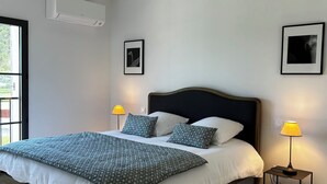 Une chambre à coucher comprenant un lit, deux lampes de chevet, un climatiseur fixé au mur et deux tableaux encadrés.