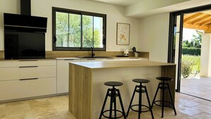 Une cuisine moderne dotée d’un grand îlot central, de tabourets de bar et d’une fenêtre donnant sur un paysage verdoyant.