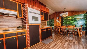 Een keuken met houten kastjes, een bakstenen muur, een inbouwoven en een eethoek met een houten tafel en stoelen.