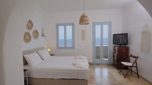 Une chambre à coucher avec un lit, une télévision, une chaise et une vue sur la mer par la fenêtre.