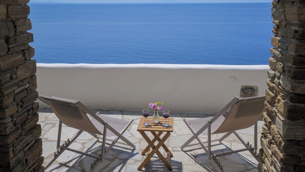 Un balcon aux murs de pierre, agrémenté de deux fauteuils et d’une petite table sur laquelle sont posés un vase de fleurs et des verres à vin.