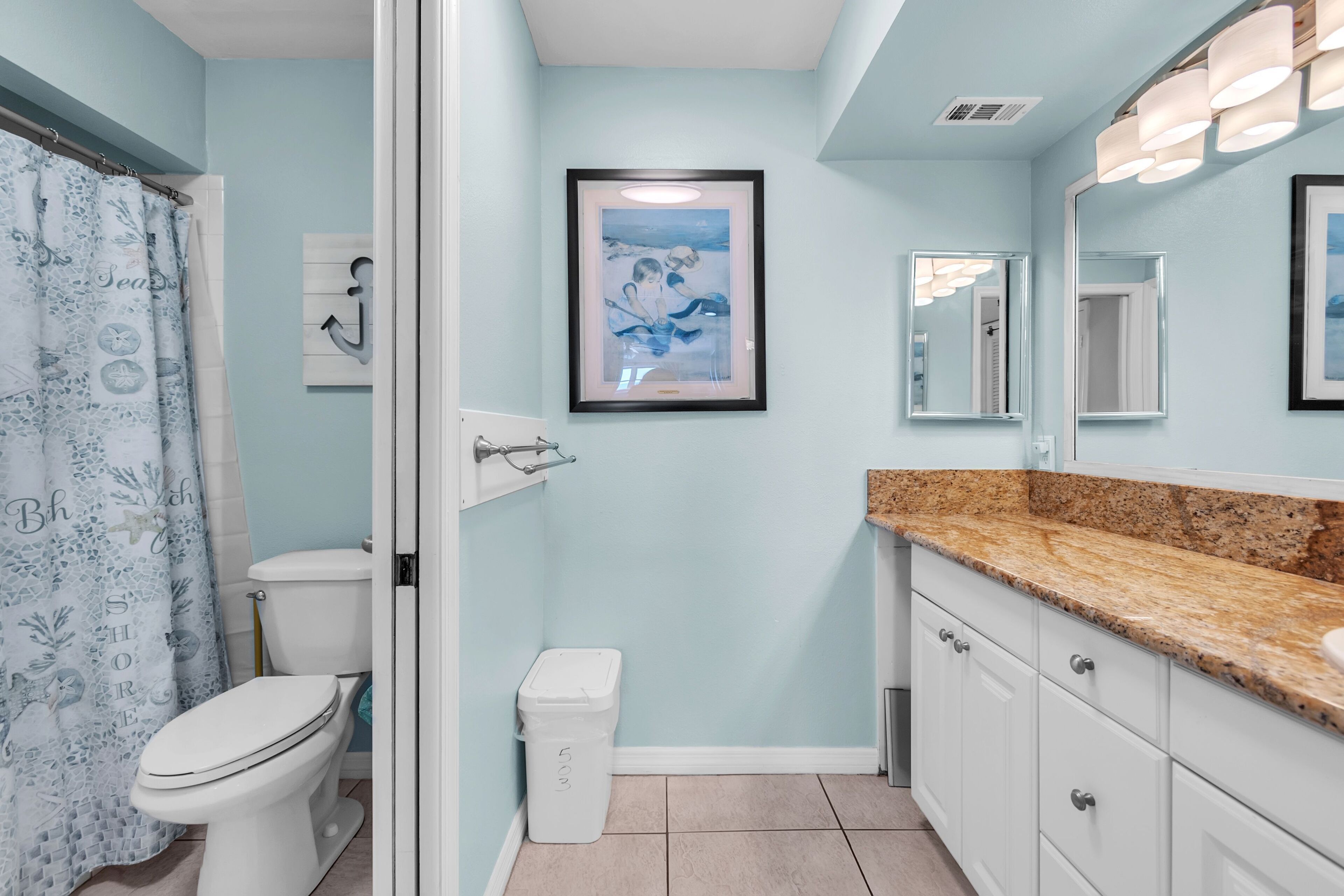 A bathroom with a toilet, a sink, a mirror, and a framed picture on the wall.