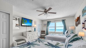 A bedroom with two beds, a ceiling fan, a TV, a dresser, a chair, and a window with curtains.