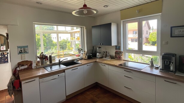 Una cocina con armarios blancos, lavavajillas, un lavabo y una ventana con vistas a un jardín.