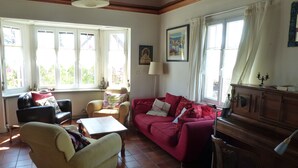 Una sala de estar con un sofá rojo, un sillón beige, un aparador de madera y una ventana con cortinas.