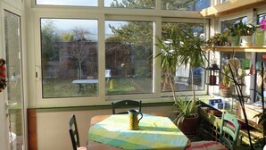 Un solárium con ventanas amplias, una mesa con sillas y varias plantas en macetas.