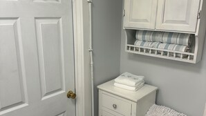 Un baño con una puerta blanca, un inodoro, un mueble con una toalla a rayas y un estante con toallas dobladas.