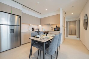 Une cuisine moderne équipée d’appareils électroménagers en acier inoxydable, une table à manger pour quatre personnes et un couloir menant à une chambre.