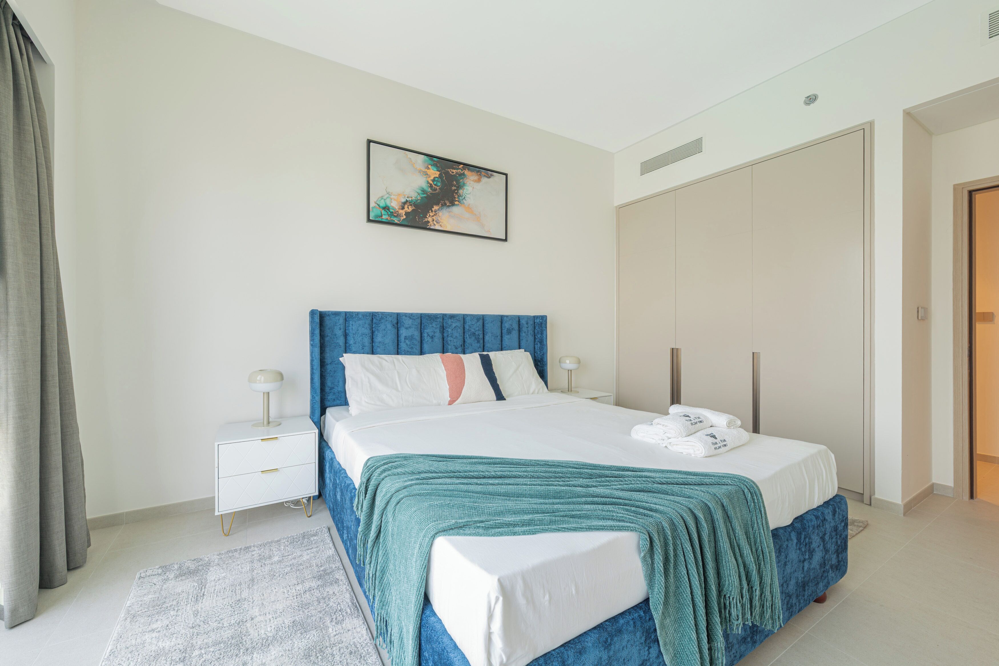 A bedroom with a bed, a nightstand, a bedside table, a wall-mounted artwork, and a wardrobe.