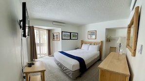 Une chambre à coucher comprenant un lit, un bureau, une chaise, un téléviseur fixé au mur et une fenêtre avec des rideaux.
