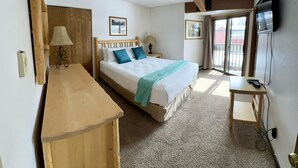 Een slaapkamer met een bed, nachtkastjes, een bureau, een plafondventilator, een televisie en een schuifdeur naar een balkon.