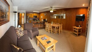 A cozy living room with a sofa, coffee table, and dining area with wooden chairs and a table. A kitchen with wooden cabinets and appliances is visible in the background. - Unit 513 - Standard Condo (Winter Park)