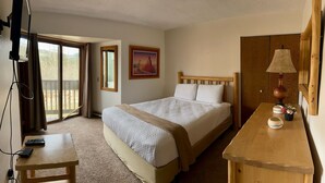 A hotel room with a bed, a desk, a lamp, a painting, and a sliding door to a balcony. - Unit 513 - Standard Condo (Winter Park)