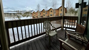A wooden deck with chairs, a view of a snow-covered landscape, and a building with multiple windows. - Unit 513 - Standard Condo (Winter Park)