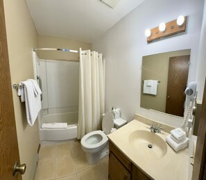 A bathroom with a shower, toilet, sink, and a mirror with lights.
