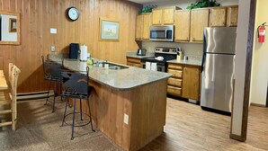 A kitchen with wooden cabinets, a stainless steel refrigerator, a microwave, a sink, and a bar stool. - Unit 521 - Standard Condo (Winter Park)