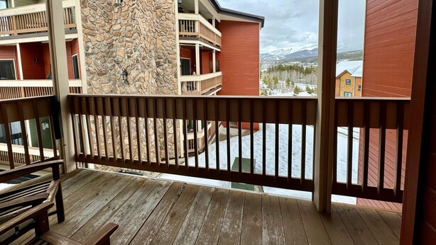 A balcony with a stone wall, wooden railings, and a view of a snowy mountain landscape. - Unit 521 - Standard Condo (Winter Park)