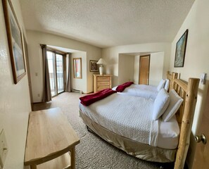 A bedroom with a large bed, wooden headboard, a wooden dresser, a desk, and a window with curtains.