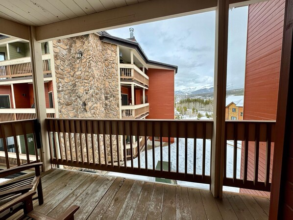 A balcony with a stone wall, wooden railings, and a view of a snowy mountain landscape.