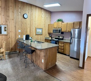 A kitchen with wooden cabinets, a stainless steel refrigerator, a microwave, and a sink. - Unit 531 - Standard Condo (Winter Park)