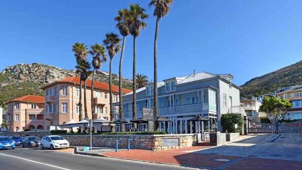 A hotel with a modern facade, a parking area, and a mountain backdrop. - Kalk Bay Condo at The Majestic (Cape Town)