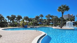 A swimming pool with a tiled deck, palm trees, and a hotel building in the background. - 3rd Floor Condo w/ Large Community Pool in Central Destin! 🌺🐬 (Destin)