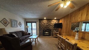 A cozy living room with a stone fireplace, a wooden dining table, and a ceiling fan. - Unit 624 - Updated Condo (Winter Park)