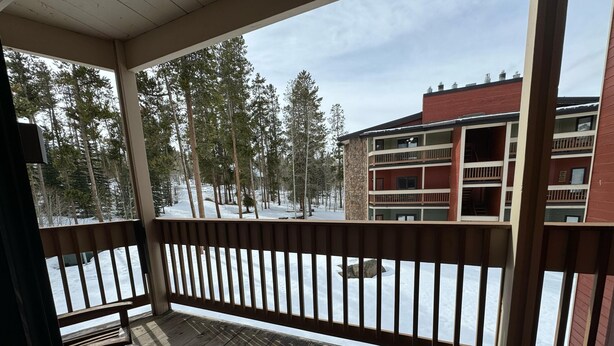 A wooden deck with a view of a multi-story building and snow-covered ground. - Unit 624 - Updated Condo (Winter Park)