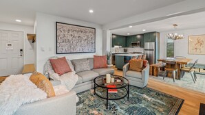 A modern living room with a grey sofa, a coffee table, and a dining area with a wooden table and chairs.