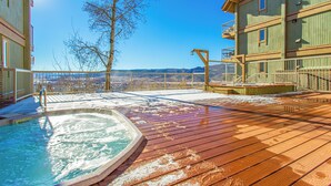 A wooden deck with a hot tub, a view of mountains, and a building with balconies.