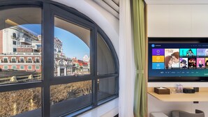 A modern room with a large window overlooking a cityscape, a flat-screen TV mounted on the wall, and a wooden desk with a chair. - MUDONG YOUTH  HOSTEL (Harbin)