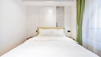 Una habitación de hotel moderna con una cama grande, un cabecero con detalles de mármol, un armario y una cortina verde.