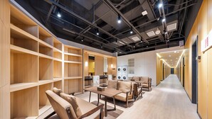 A hotel lobby with wooden shelving units, a seating area with sofas and tables, and a visible laundry facility. - MUDONG YOUTH  HOSTEL (Harbin)