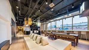 A modern office space with a long sofa, bar area, and large windows overlooking a bridge. - MUDONG YOUTH  HOSTEL (Harbin)