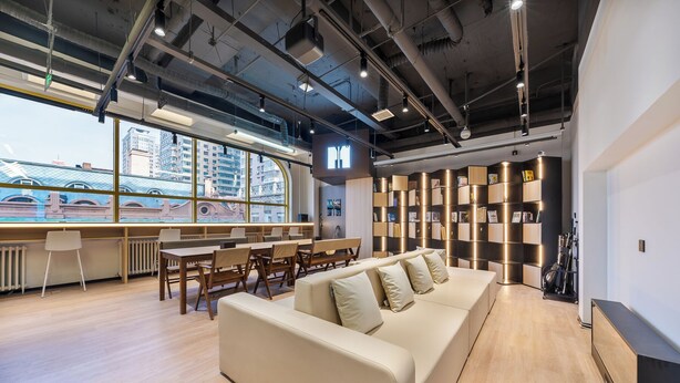 A modern office space with a large window, a sofa, tables, chairs, and a bookshelf. - MUDONG YOUTH  HOSTEL (Harbin)