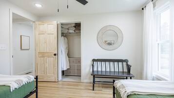 A bedroom with two beds, a wooden wardrobe, a bench, a mirror, and a window.
