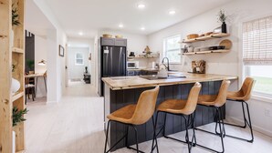 Una cocina moderna con una isla central, taburetes de bar y estanterías empotradas.