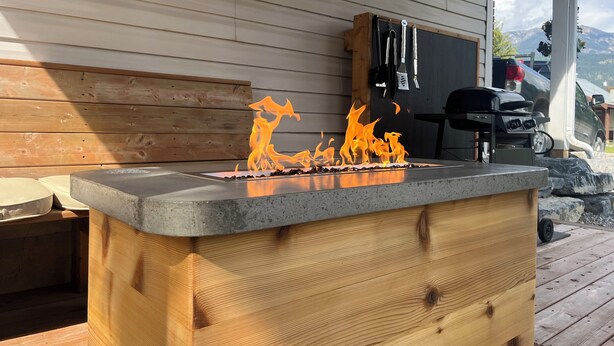 Un barbecue avec des flammes, un banc en bois et un gril en arrière-plan.