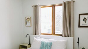 Une chambre à coucher avec un lit, une fenêtre avec des rideaux, une table de chevet avec une lampe et un tableau accroché au mur.