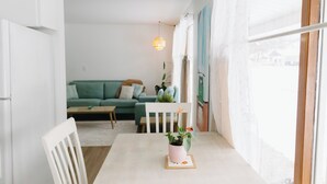 Un salon lumineux avec une table blanche, un canapé vert et une chaise blanche.