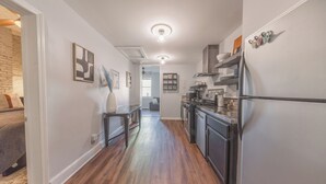 A narrow kitchen with wooden flooring, a refrigerator, and a dining area with a table and chairs.