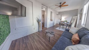 A modern living room with a grey sofa, a ceiling fan, and a dining area with a table and chairs.