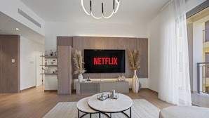 A modern living room with a large flat-screen TV displaying "NETFLIX" in red letters, a round marble coffee table, and a minimalist design.