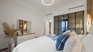 A modern bedroom with a large bed, a dresser, a vanity, and a large window with a view.